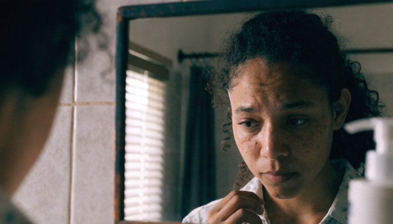 Mulher olhando o próprio reflexo no espelho com expressão incerta e autocrítica