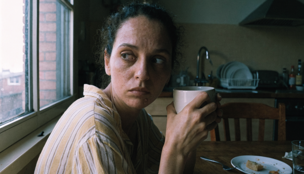 Mulher à mesa da cozinha pela manhã, segurando a xícara de café com as duas mãos, exausta