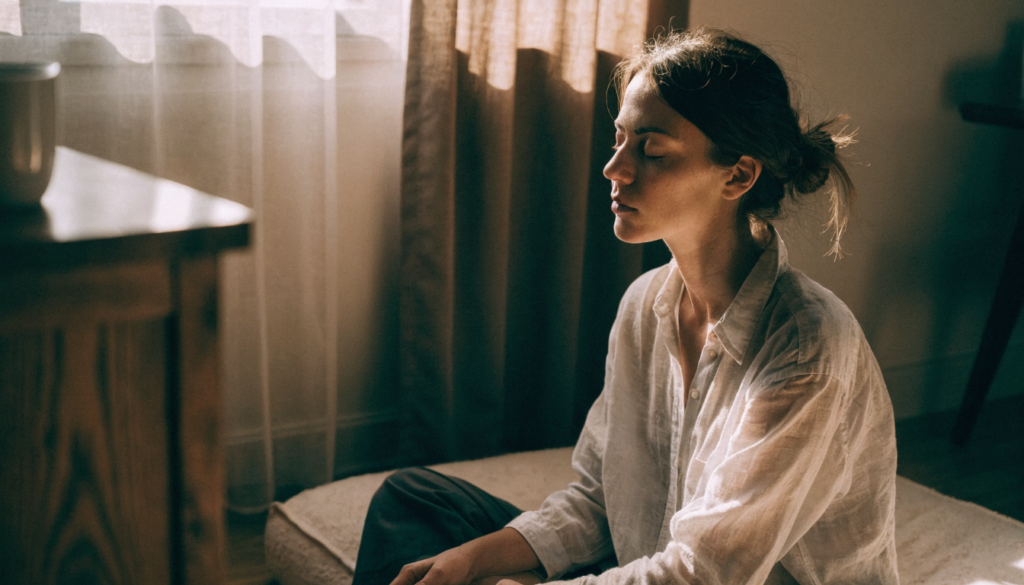 Mulher meditando de olhos fechados sentada em almofada no chão de casa