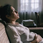 Mulher no sofá de olhos fechados com a mão na barriga, respirando devagar para se acalmar
